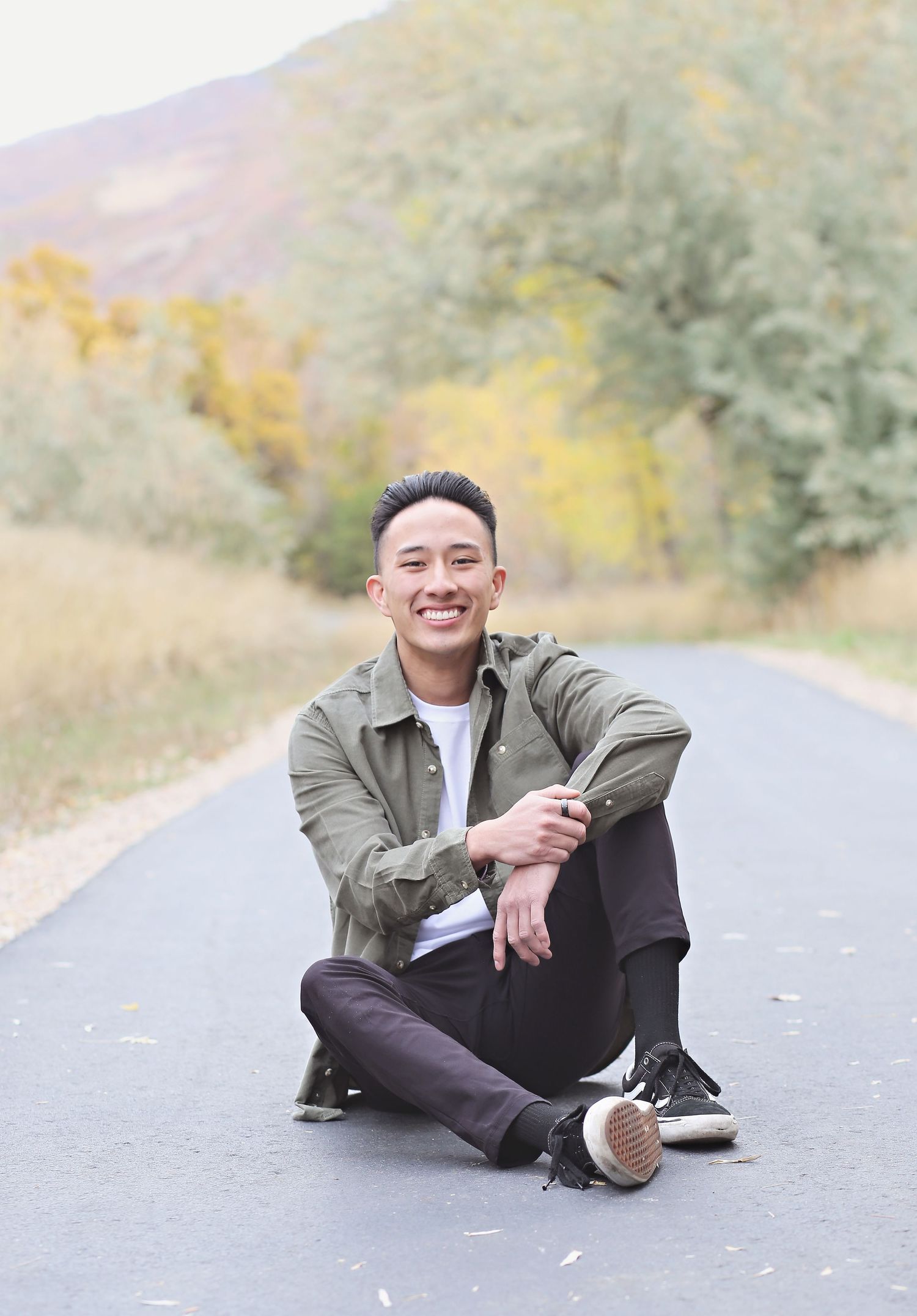 A casual portrait of someone sitting cross-legged on an autumn mountain road.