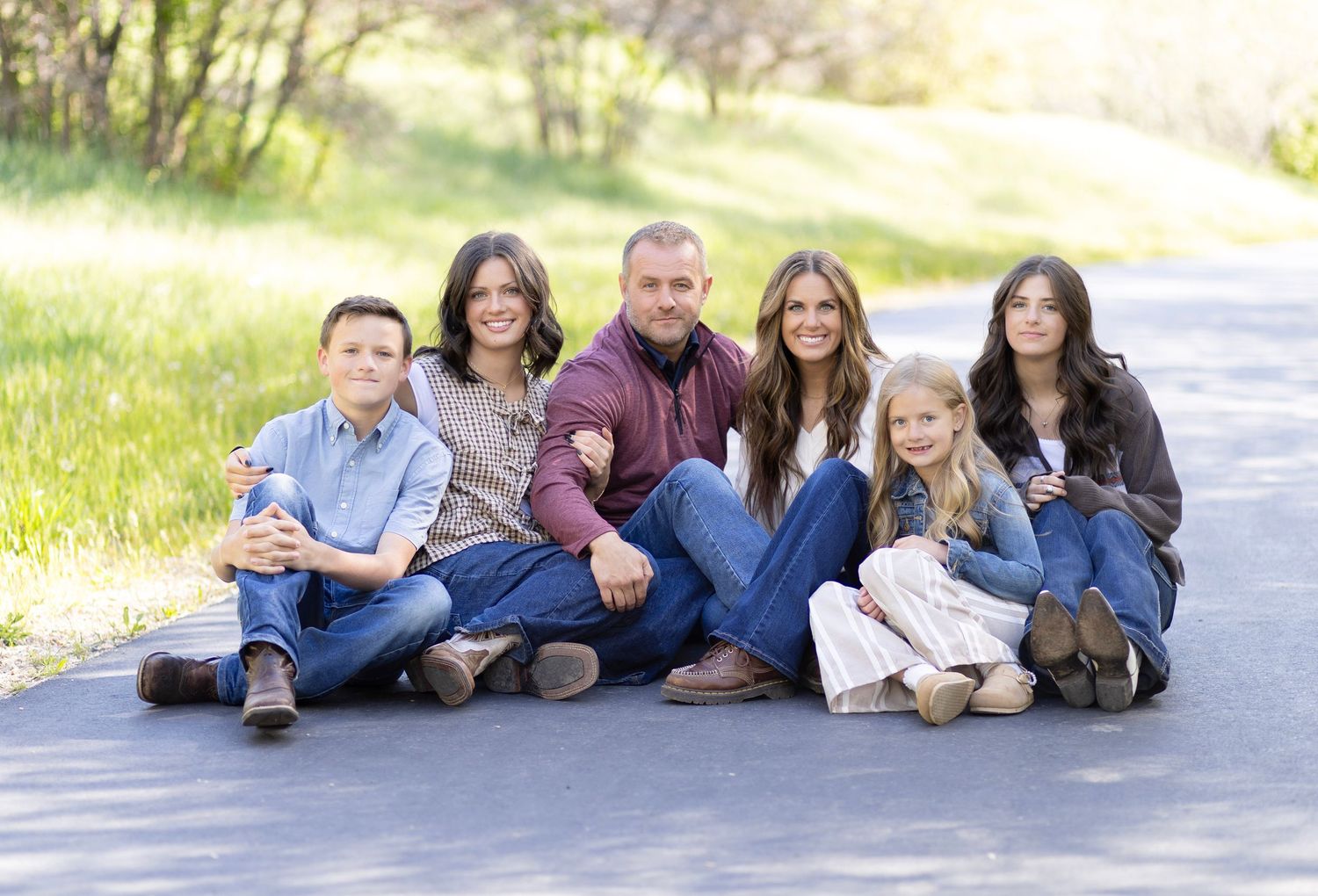 Family of seven posing together on a tree-lined road, smiling warmly in a casual outdoor portrait.