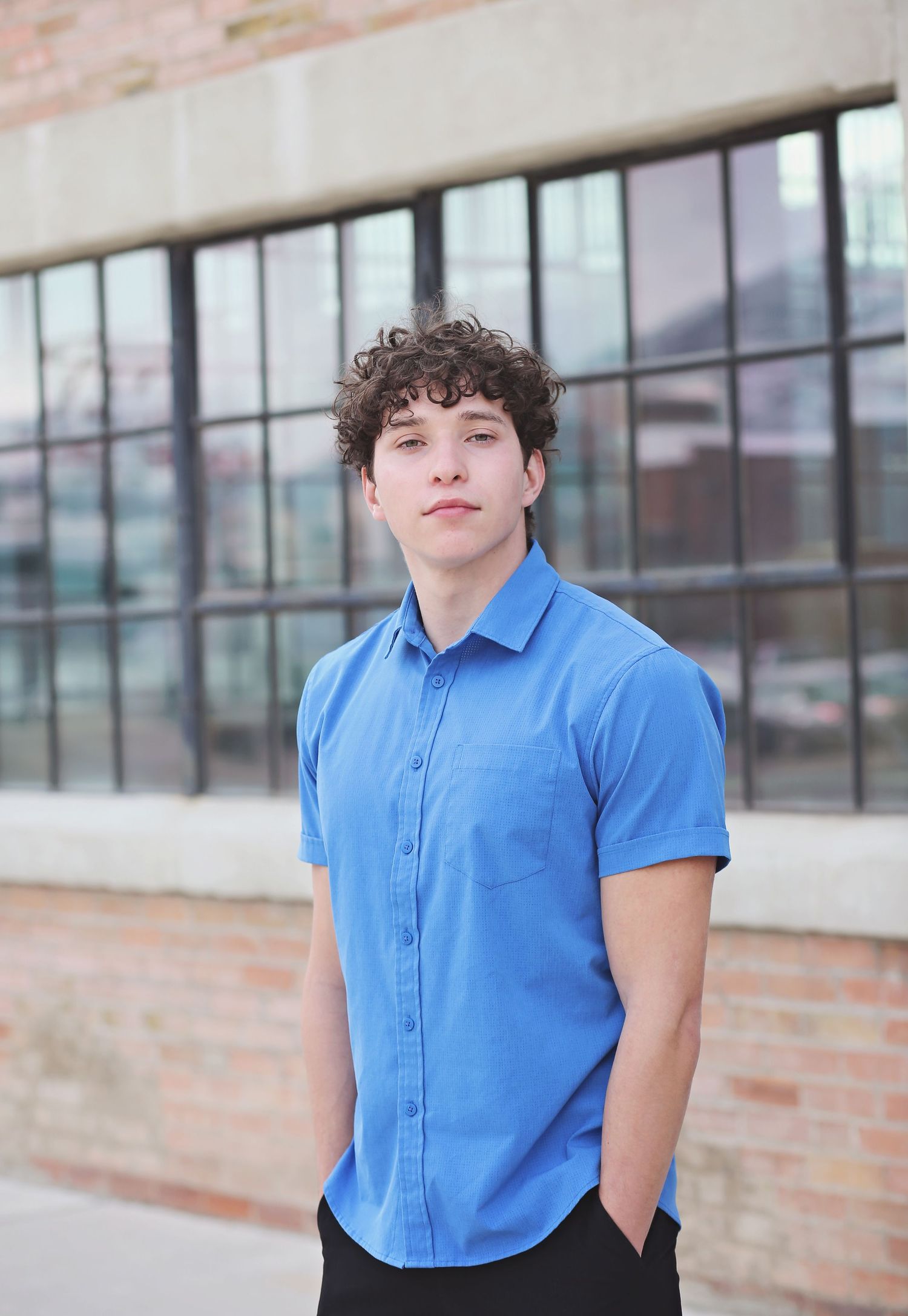 Portrait against brick wall wearing bright blue polo shirt in urban setting.