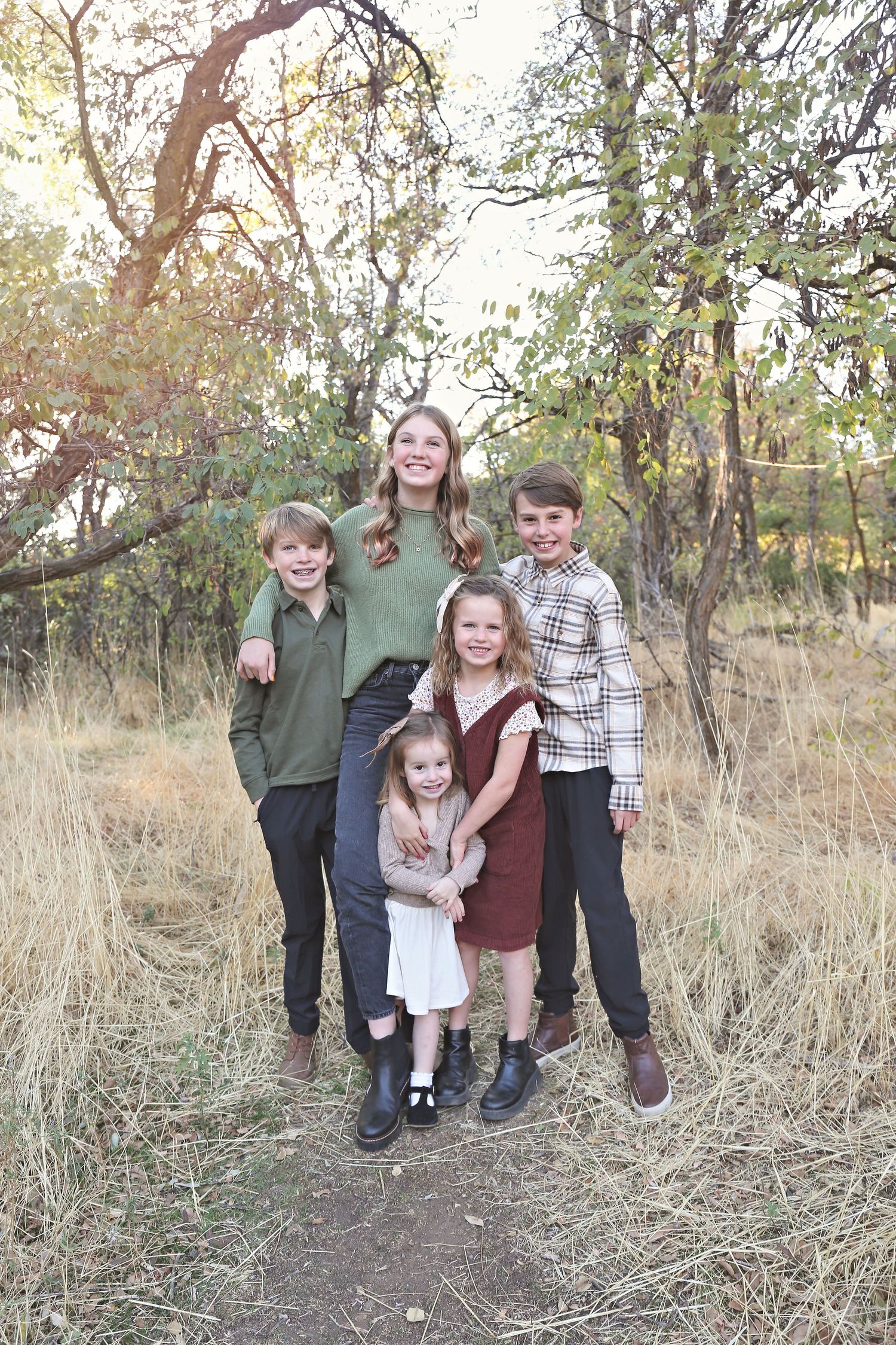 Five children pose together outdoors in coordinated outfits among tall grass.