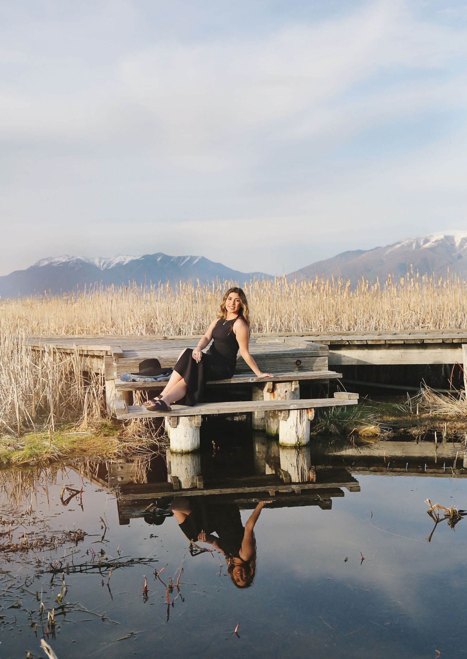 Scenic mountain landscape reflected in water with wooden dock and tall reeds.