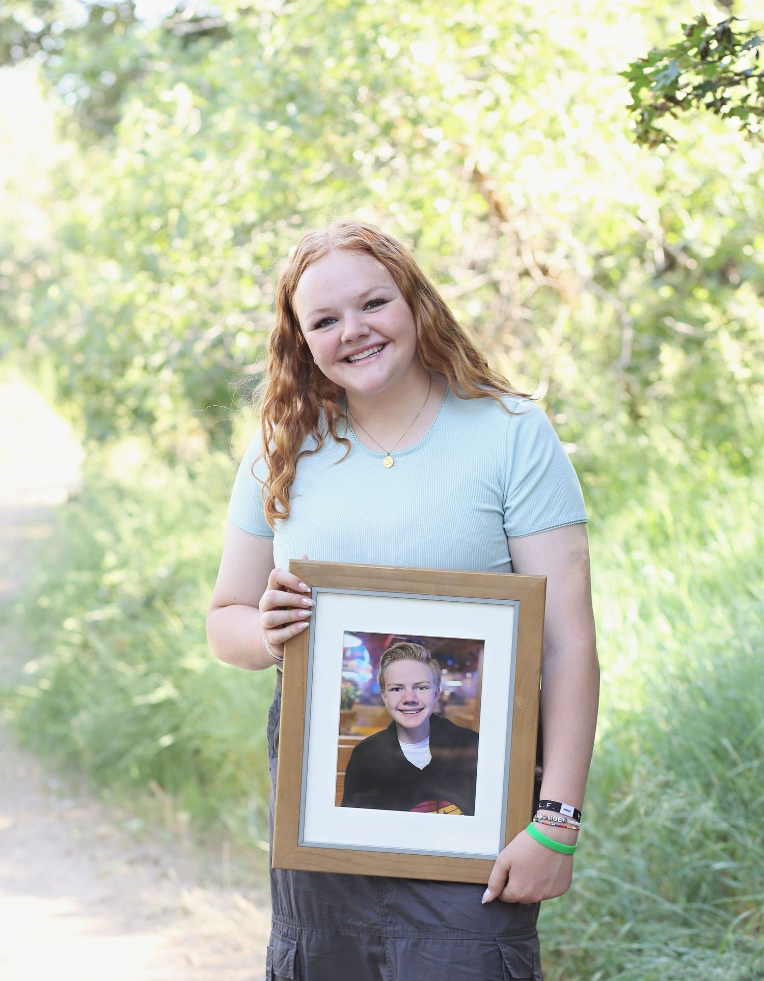 A person in a light blue shirt holds a framed photograph outdoors on a sunny day.