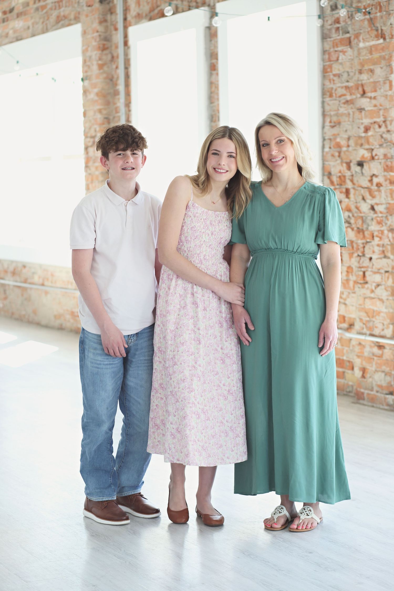 Three people in coordinated outfits pose together against a brick wall in a bright indoor setting.