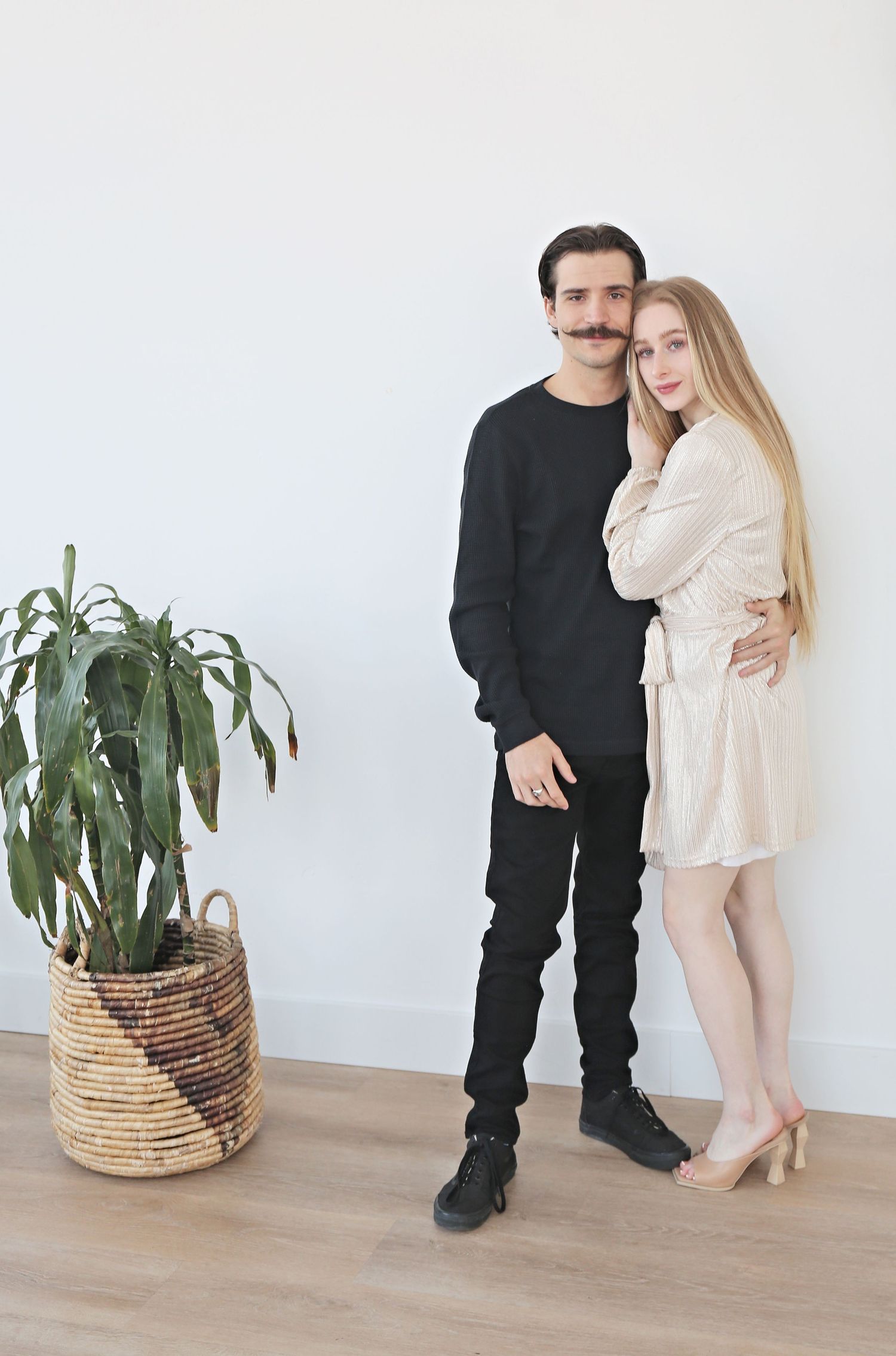 Couple poses by indoor plant in minimalist setting wearing contrasting black and cream outfits.