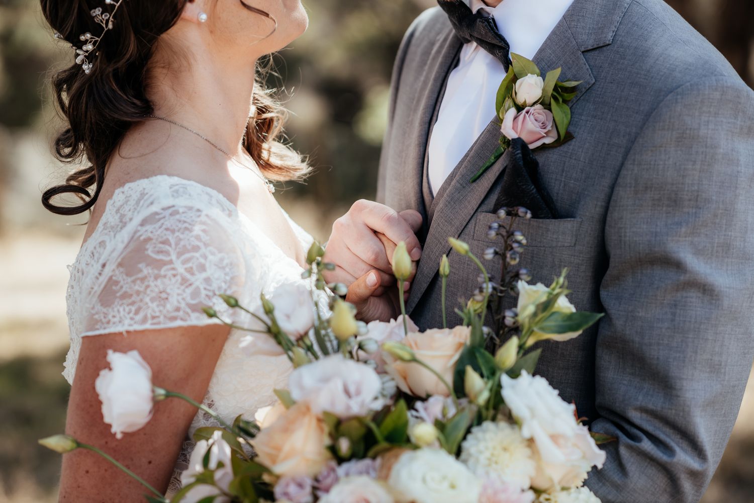 Close up of a wedding couple holding a romantic bouquet with white and peach flowers against gray suit by August and Vine