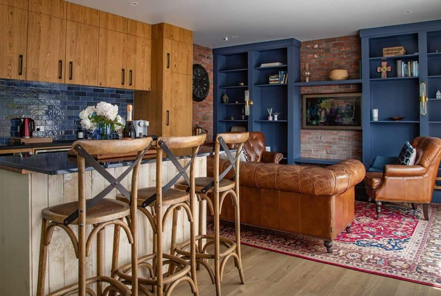 Modern interior with navy blue walls, wooden kitchen cabinets, bar stools, and a brown leather couch at Lismore Barn by August and Vine