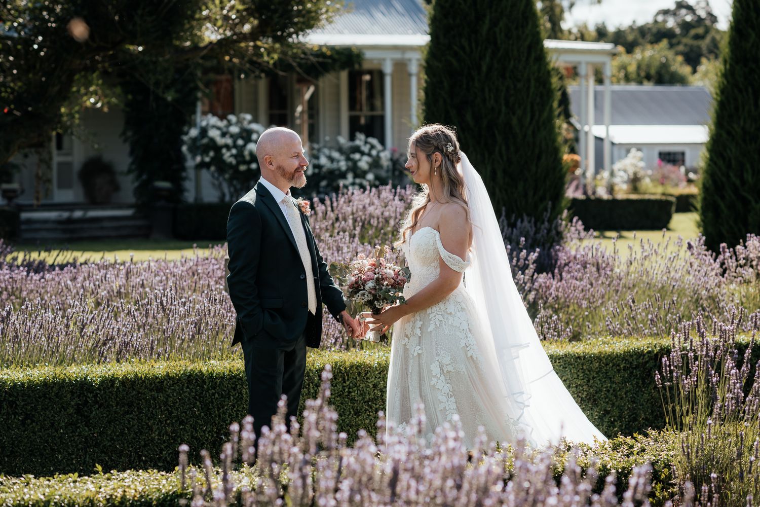 A wedding couple stand together in a beautiful garden of lavender and hedges on a sunny day at Lacewood Wairarapa by August and Vine