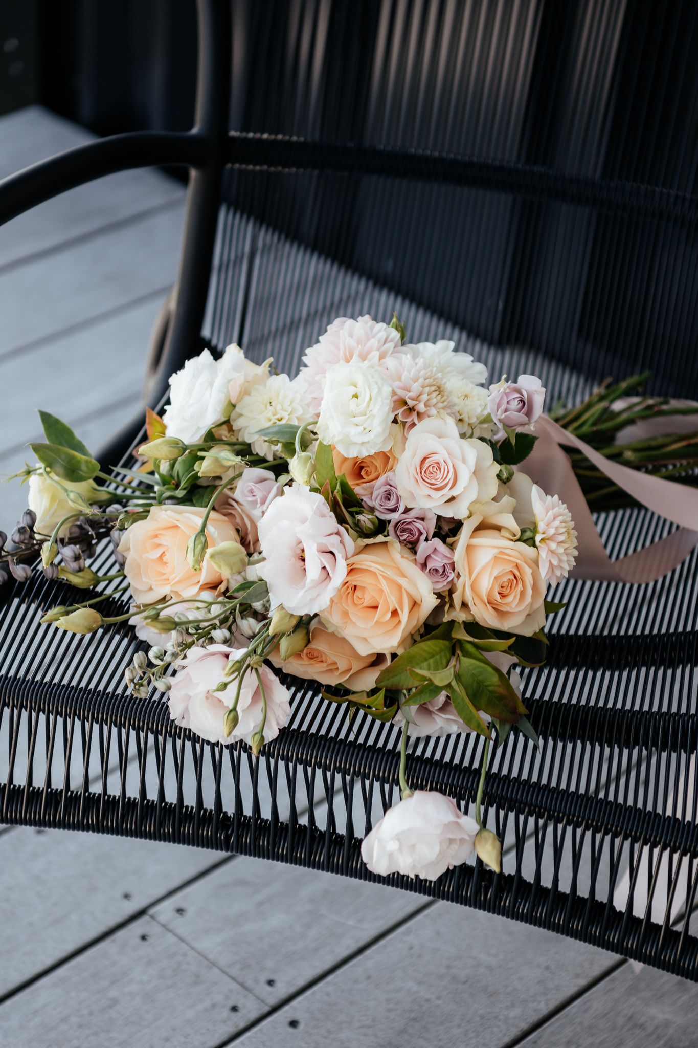 A romantic bouquet of peach and blush roses with greenery arranged on a black geometric surface by August and Vine