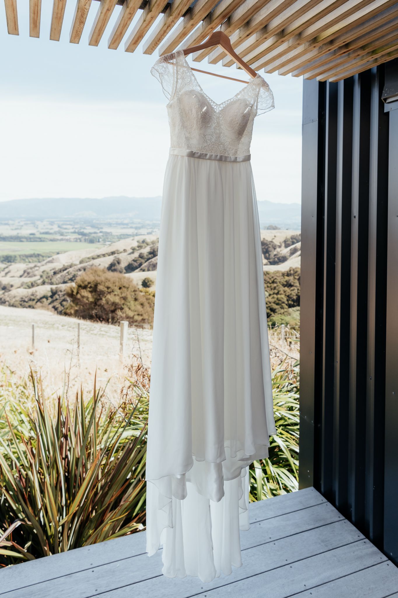 Elegant white wedding dress hangs on porch overlooking scenic mountain landscape at Whitimanuka by August and Vine