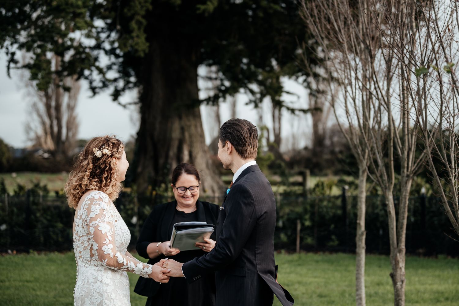 A couple exchange vows during an intimate outdoor wedding ceremony with an officiant in a Wairarapa garden setting by August and Vine