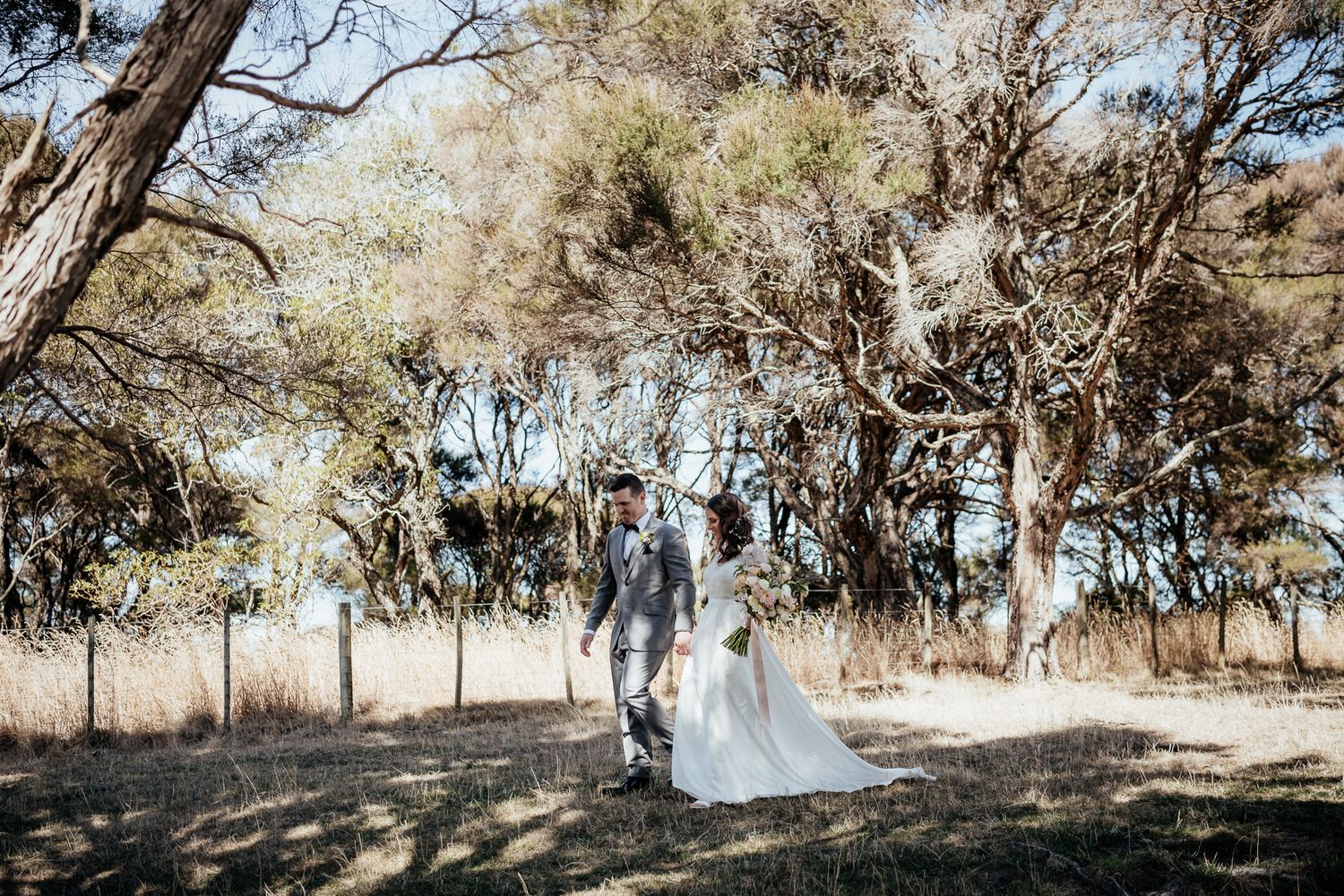 A couple walks hand in hand through Manuka with dappled sunlight filtering through at Whitimanuka by August and Vine