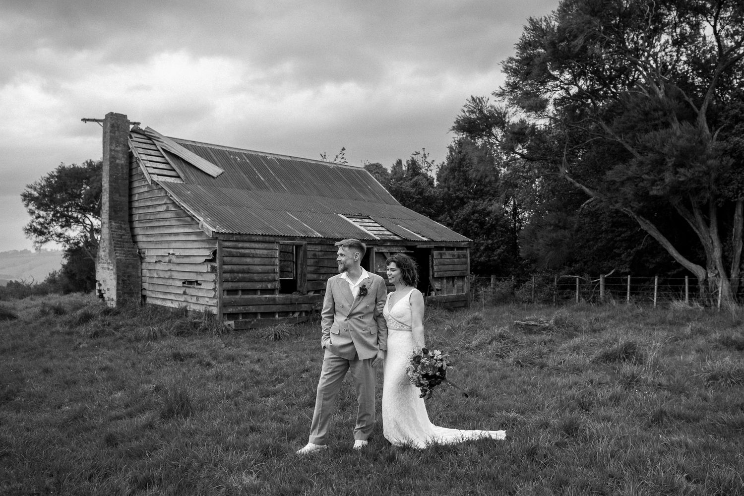 A black and white wedding photograph showing a couple in a rustic Wairarapa setting in front of an old ruin by August and Vine