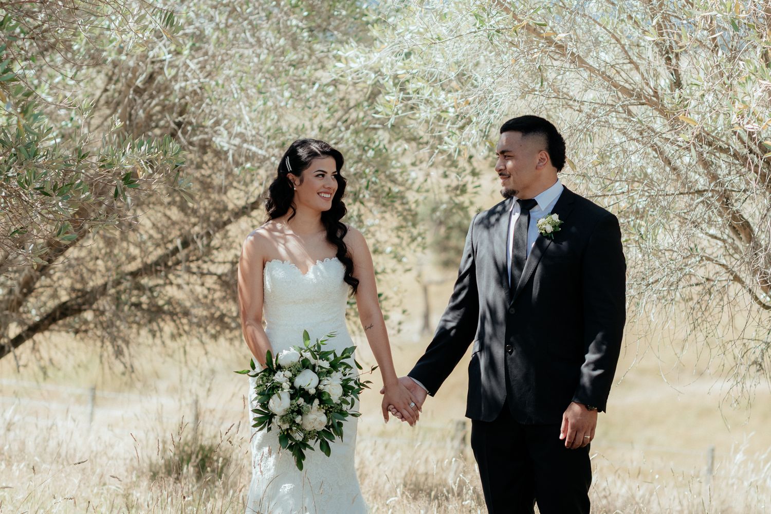 Bride and groom Asafo Aumua hold hands under olive trees at their Martinborough summer wedding by August and Vine
