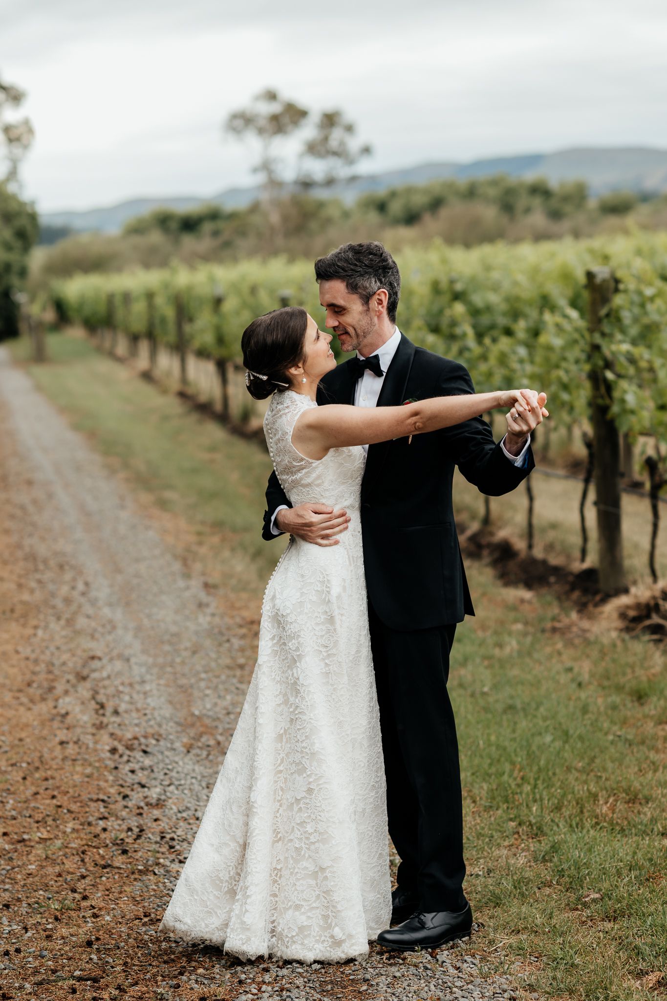 A wedding couple dance together on a path between rows of grapevines in a scenic Wairarapa vineyard by August and Vine
