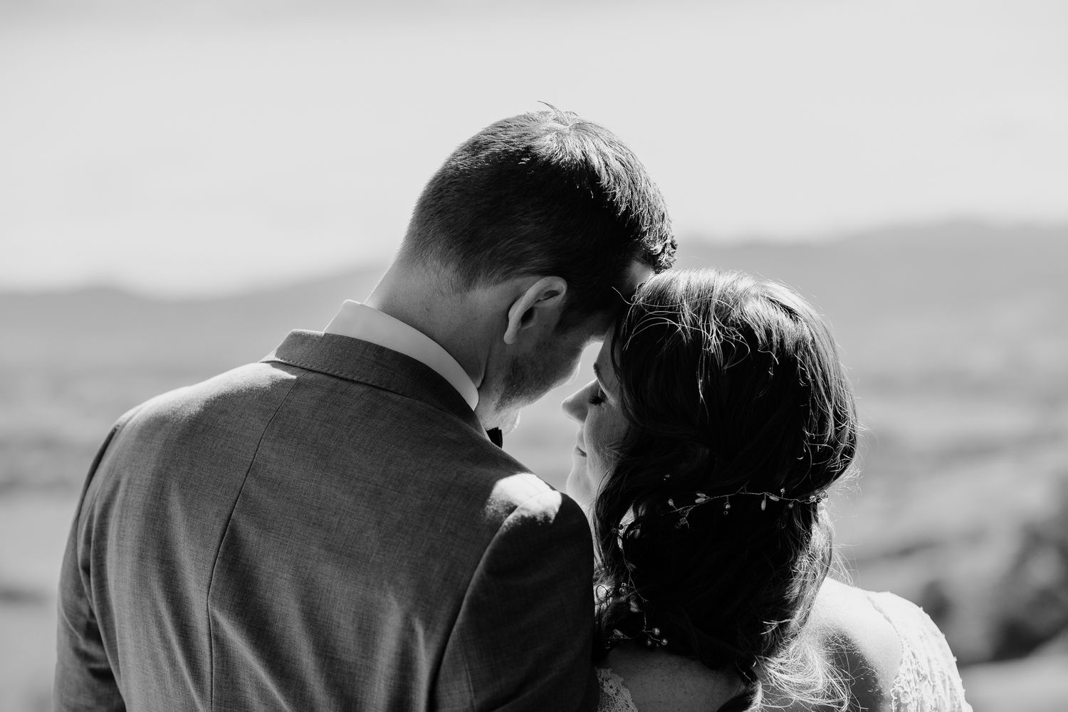 Black and white romantic portrait of a couple sharing an intimate moment against a scenic mountain backdrop by August and Vine