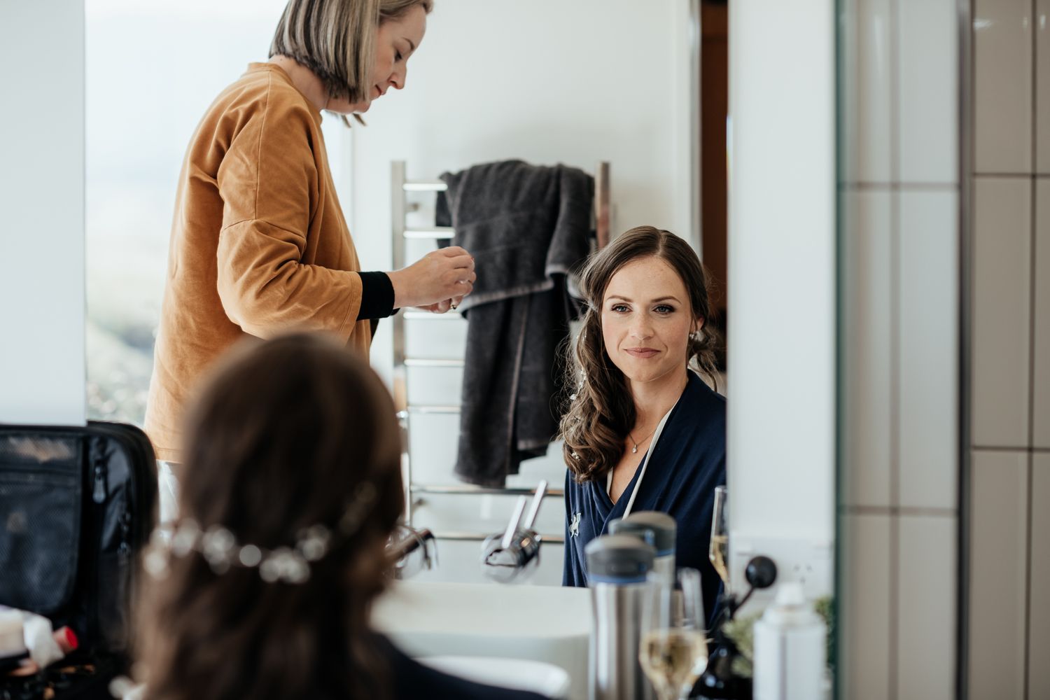 Makeup Artist works on bride in bathroom with mirrors at Whitimanuka by August and Vine