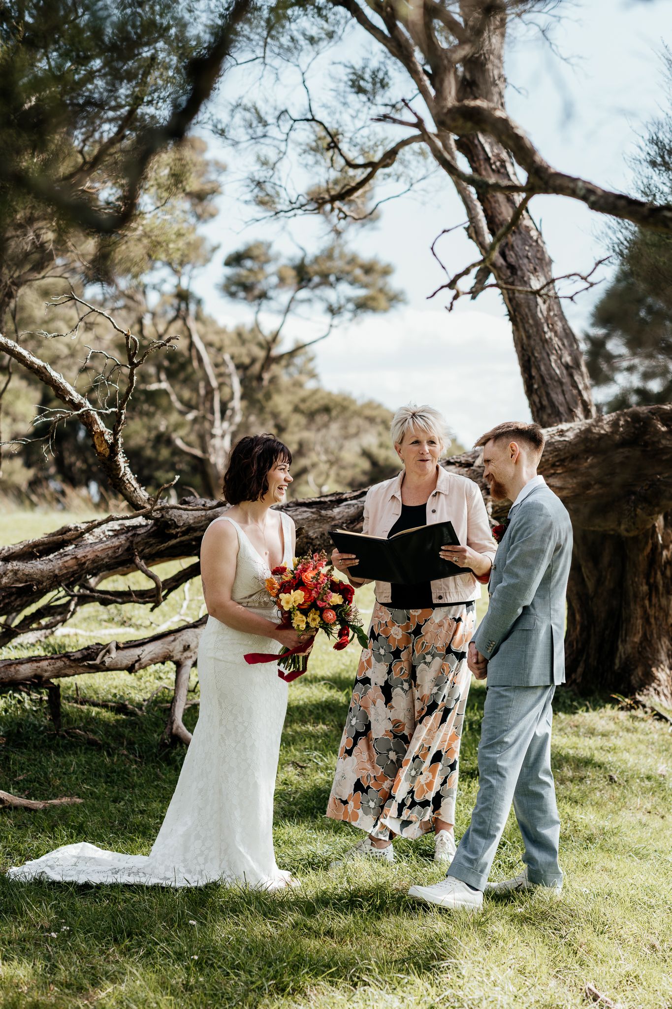 Intimate outdoor wedding ceremony under a tree with a couple exchanging vows and an officiant presiding over the service by August and Vine