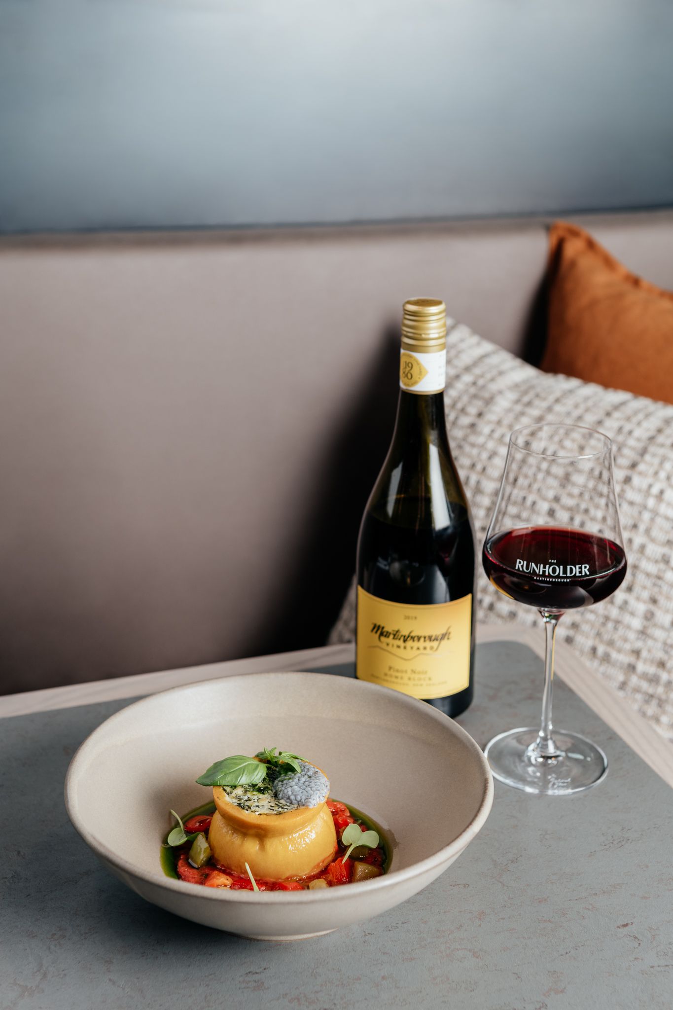 An elegantly plated dish and wine glass arranged on a gray table at The Runholder by August and Vine