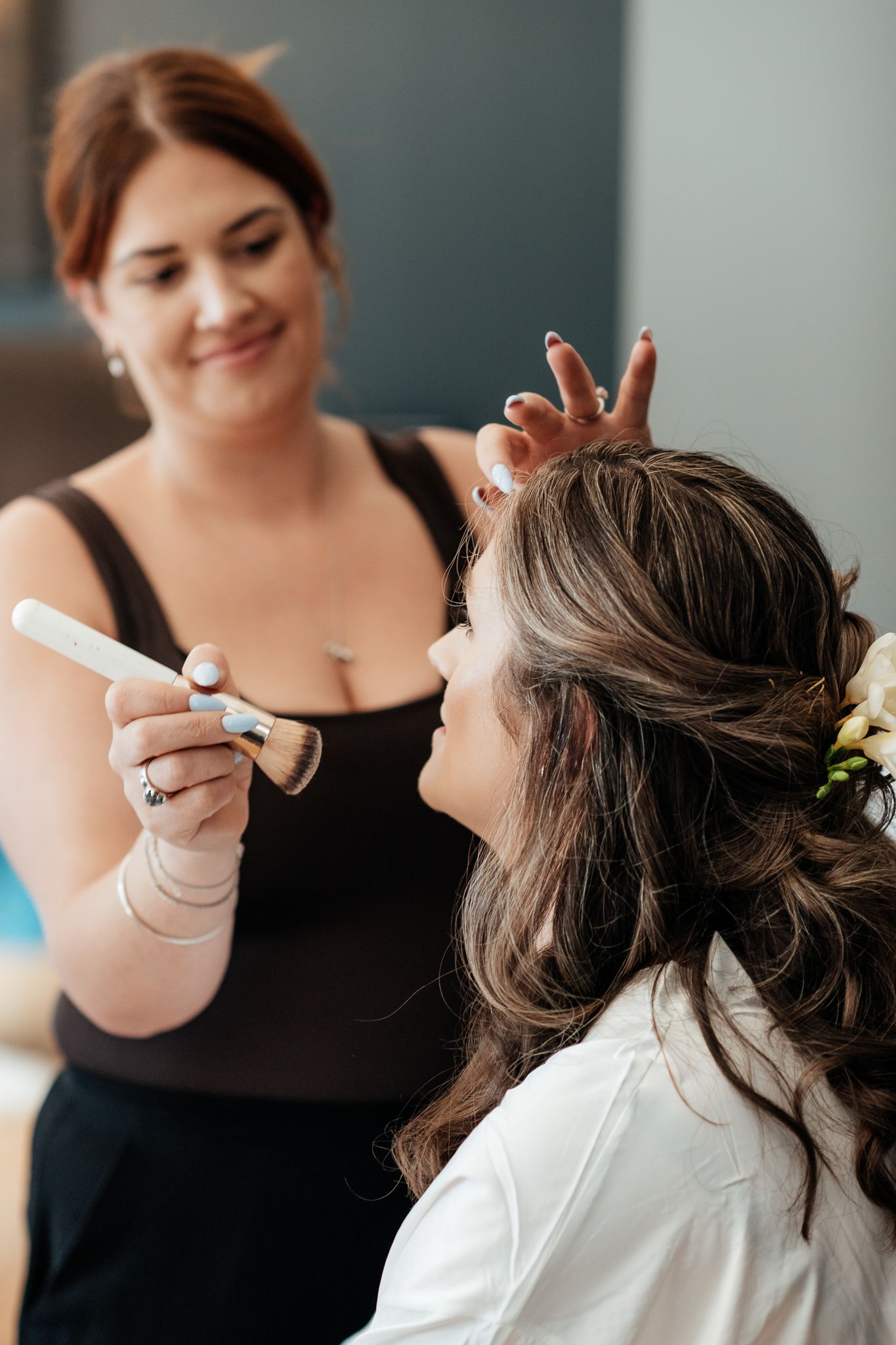 A bride getting her makeup professionally applied while wearing a white top by August and Vine