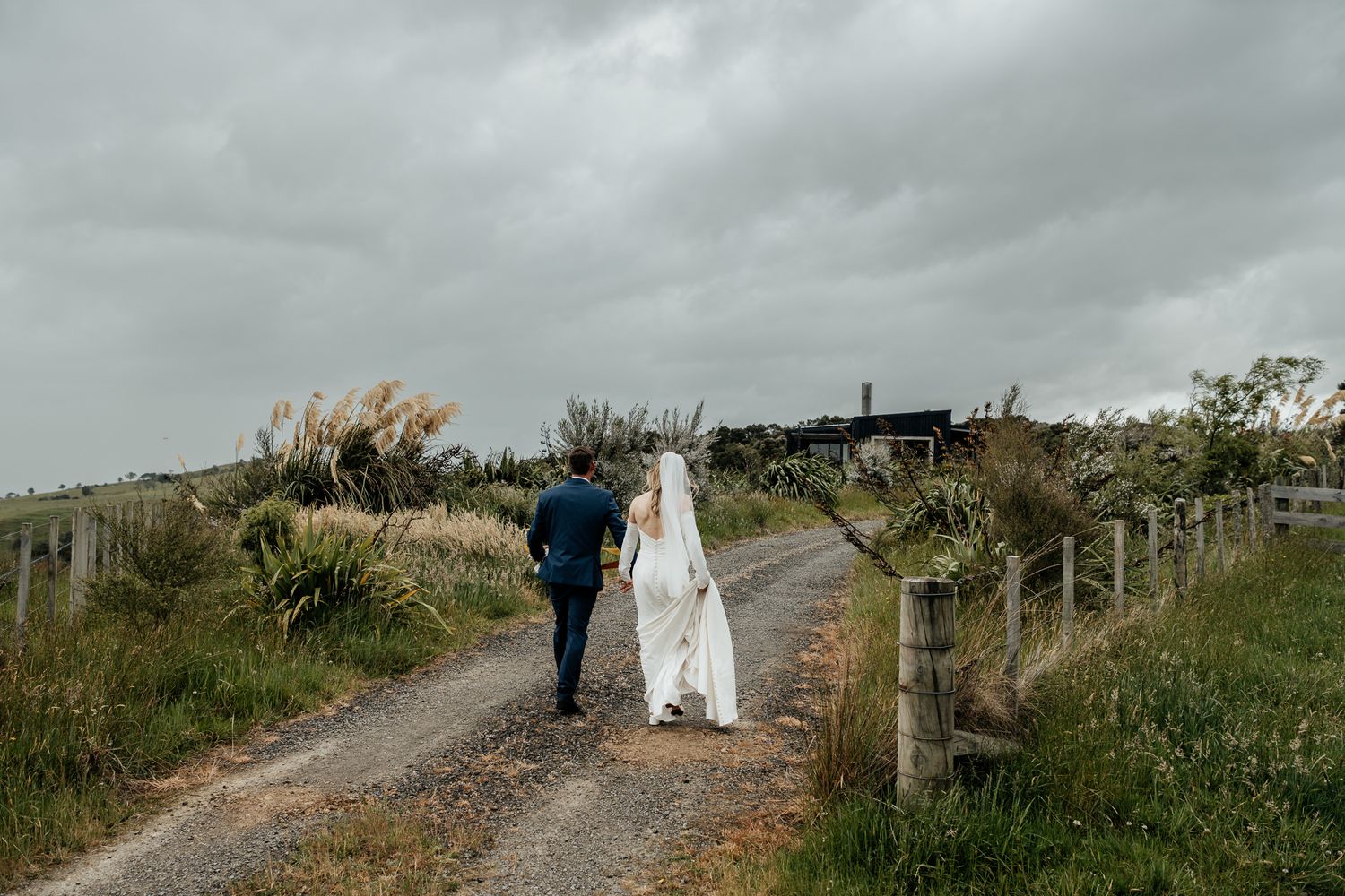 Couple walking on a rustic path through green coastal hills on an overcast day at Whitimanuka Wairarapa by August and Vine