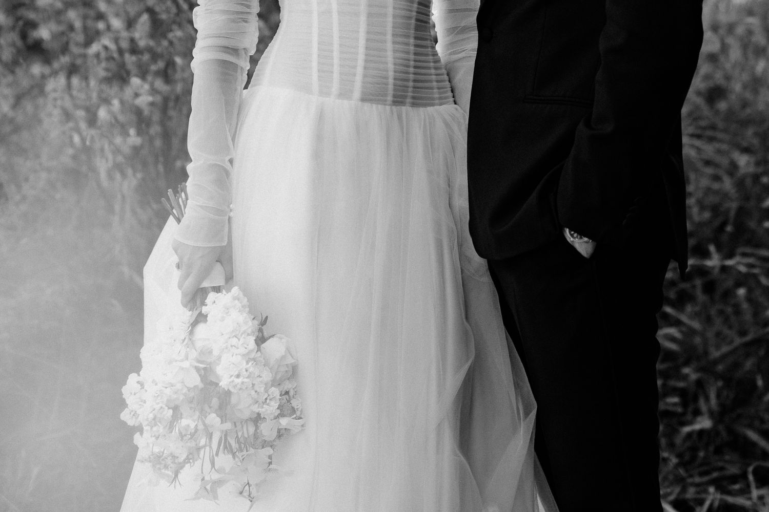 Close up waist down of wedding couple in luxury formal attire, captured in black and white photography by August and Vine