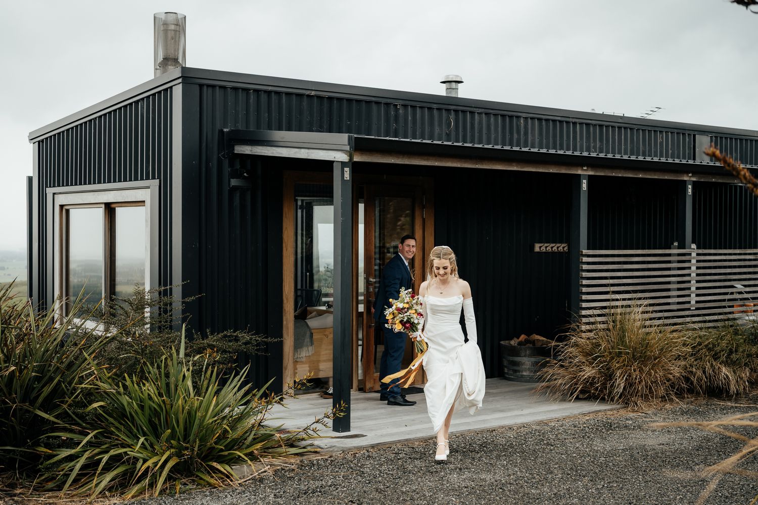 Bride and Groom exit a modern black-clad off-grid contemporary building at Whitimanuka Wairarapa by August and Vine