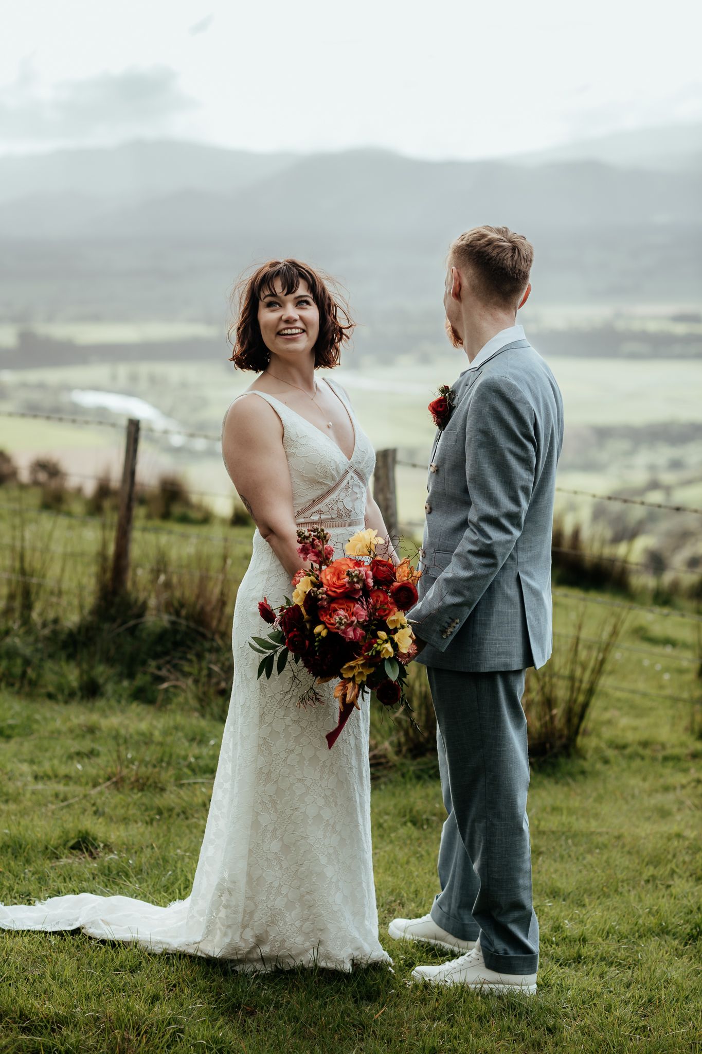 A wedding couple shares an intimate moment on a grassy hillside with scenic mountains in the background by August and Vine