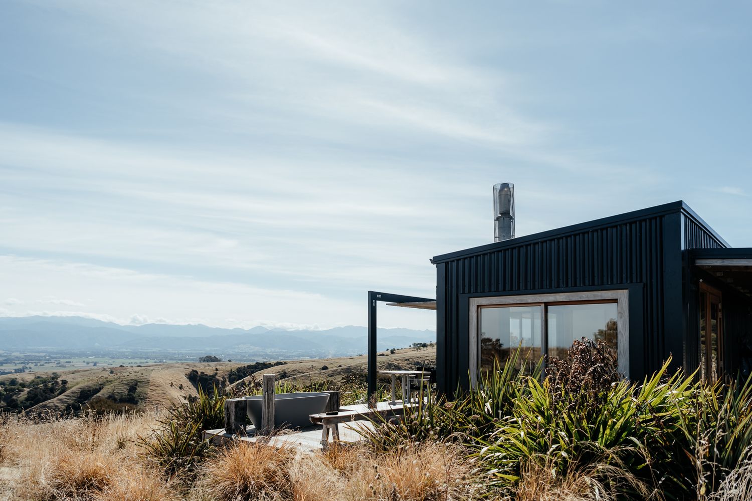 Modern black cabin with large windows on a hill overlooking mountains and native grasses in the country at Whitimanuka by August and Vine