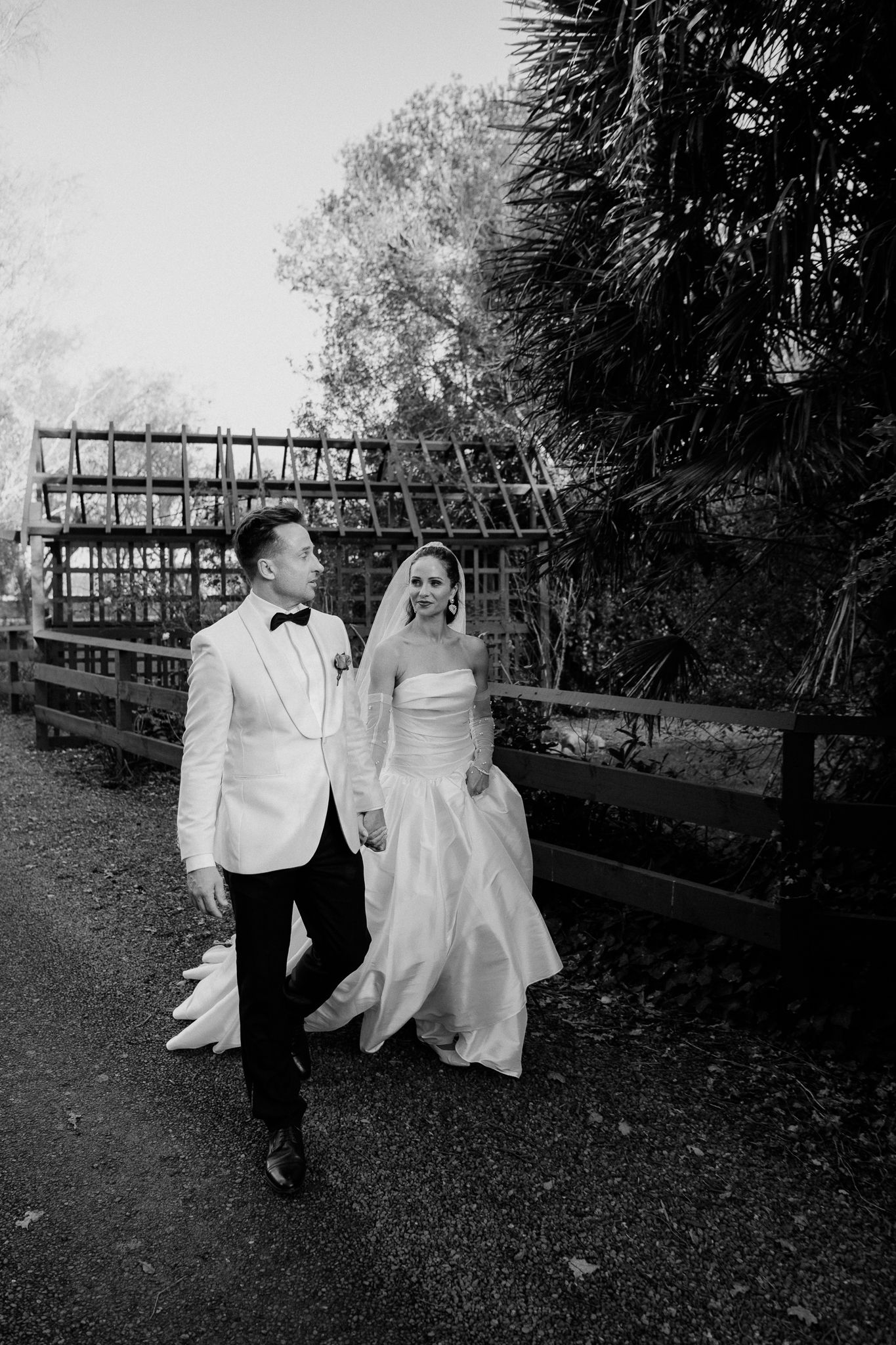 A bride and groom walking together along an outdoor path in black and white at Tarureka Estate by August and Vine