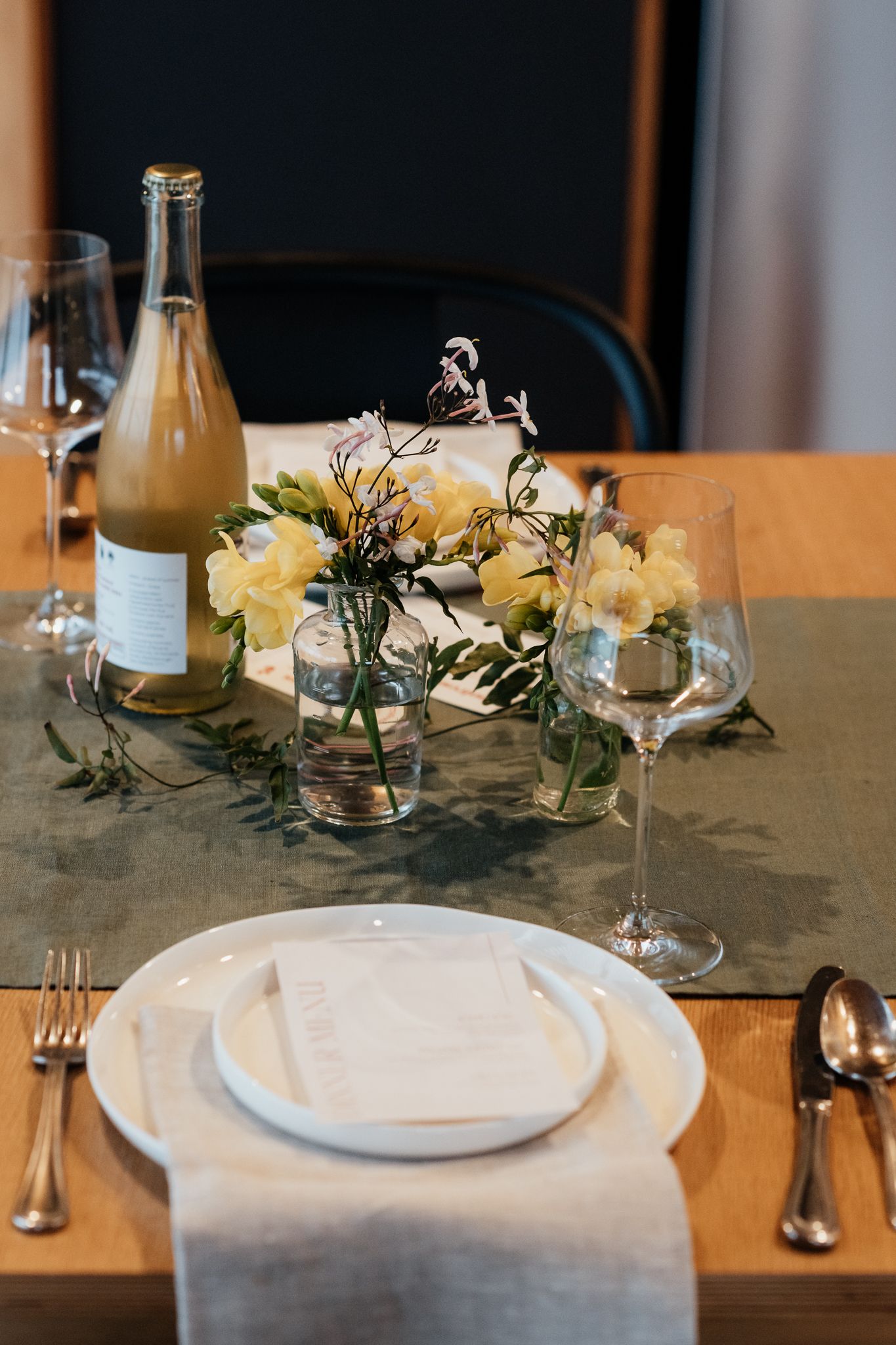 Elegant table setting with white plates, glassware, and delicate floral centerpieces featuring white roses and greenery by August and Vine