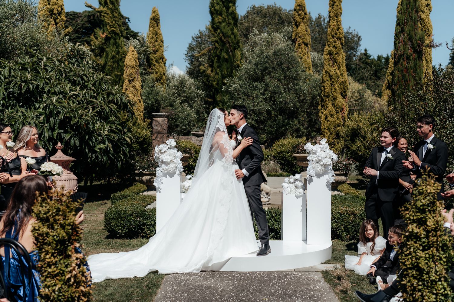 A beautiful modern outdoor garden wedding ceremony at the Milk Station Otaki with cypress trees and lush greenery by August and Vine