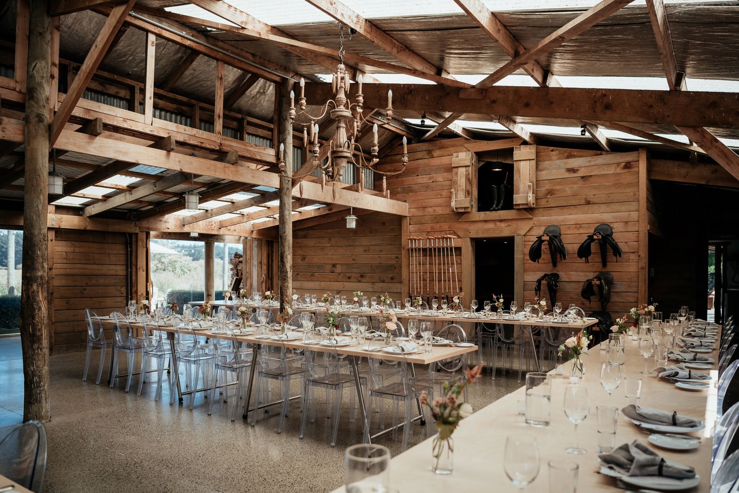 A rustic wooden barn wedding reception venue under exposed beams with long tables with elegant place settings at Sudbury by August and Vine