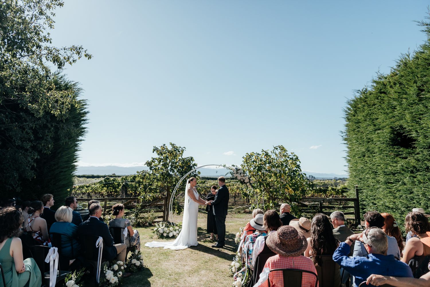 Outdoor wedding ceremony at 3 Little Words Martinborough with guests seated on both sides of a floral arch by August and Vine