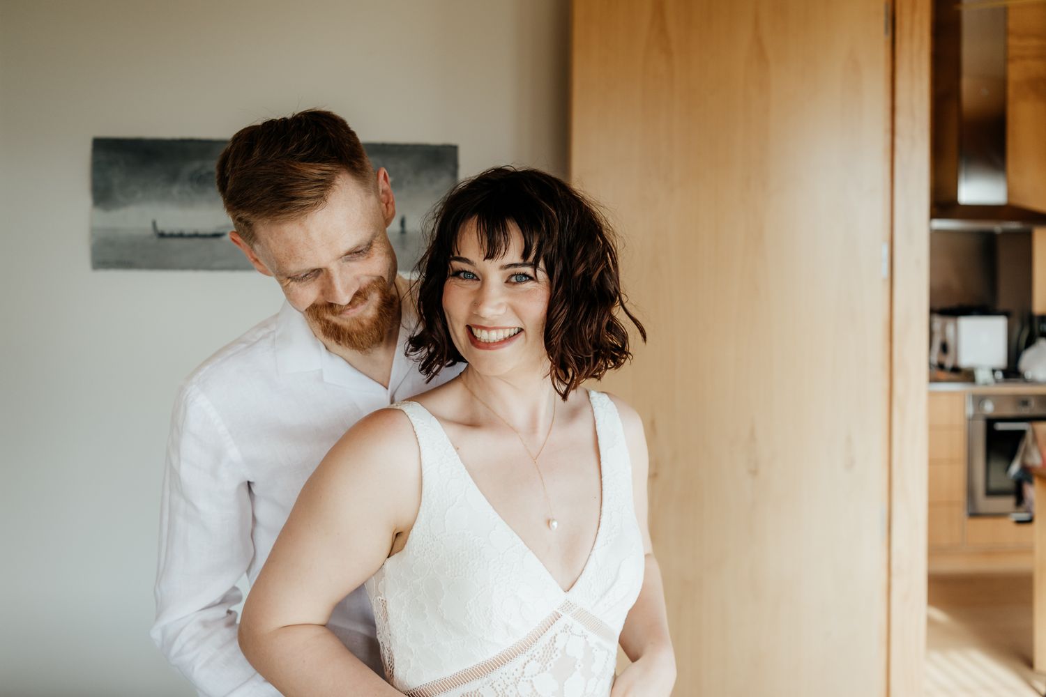 A couple in wedding attire embrace intimately in a bright indoor setting with warm lighting and neutral tones by August and Vine