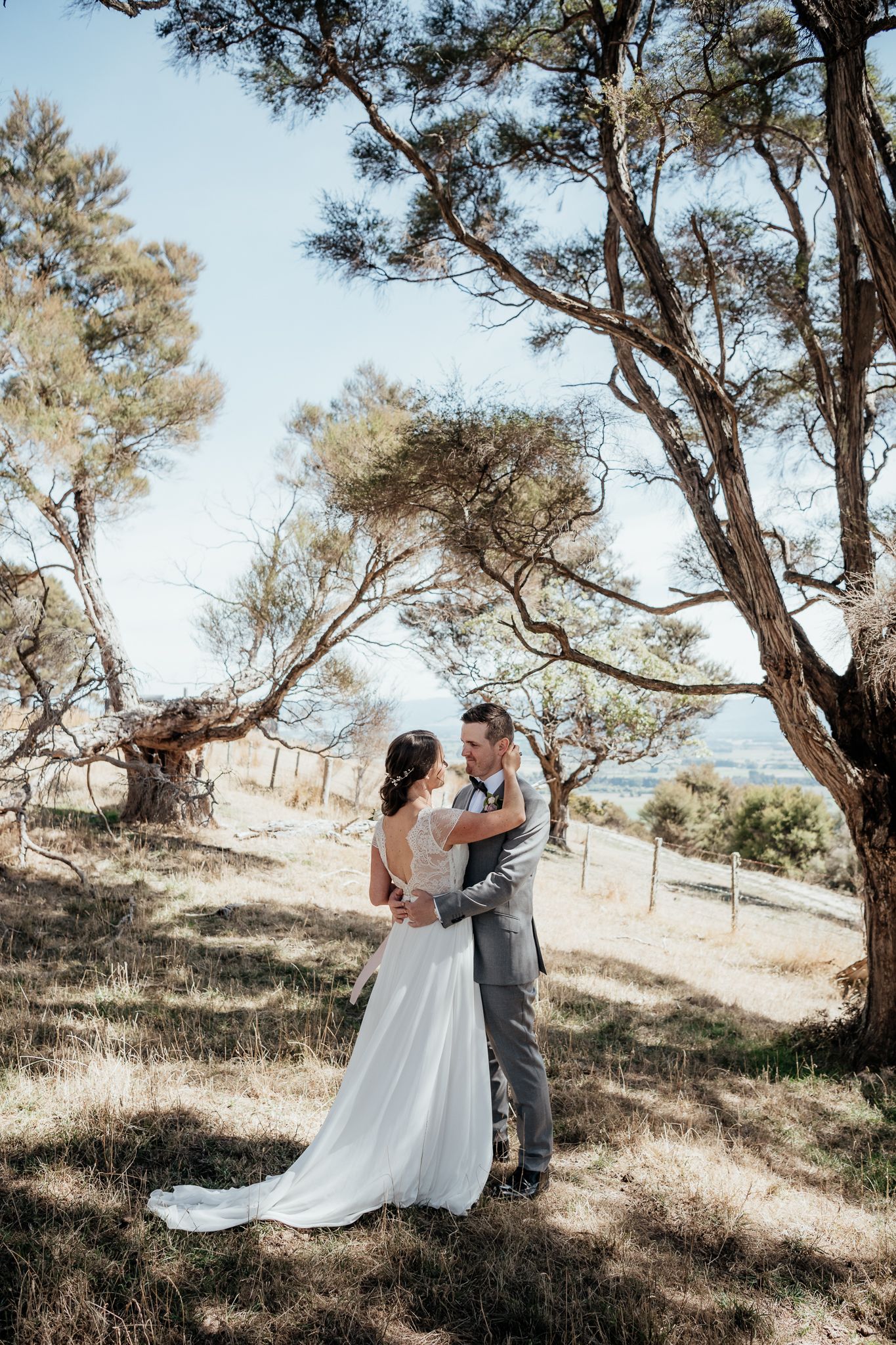 Newlywed couple share an intimate moment under tall trees on a hillside during their elopement at Whitimanuka by August and Vine