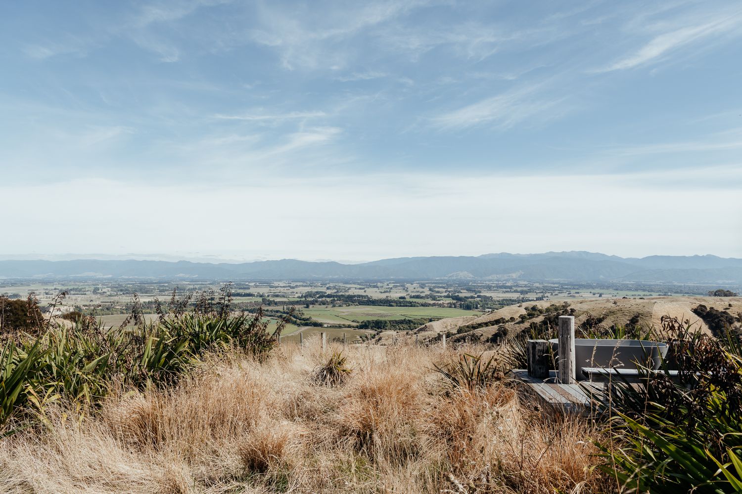 Scenic hilltop vista overlooking rolling hills and valleys with dried grass under a blue sky at Whitimanuka by August and Vine
