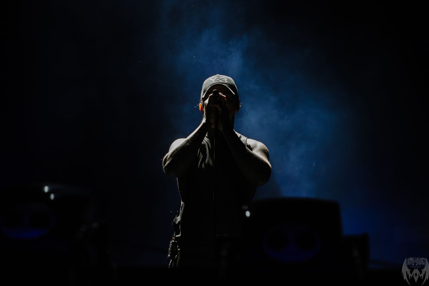A dark silhouette of a figure appears against a dramatic blue backlit background creating a moody atmospheric scene.