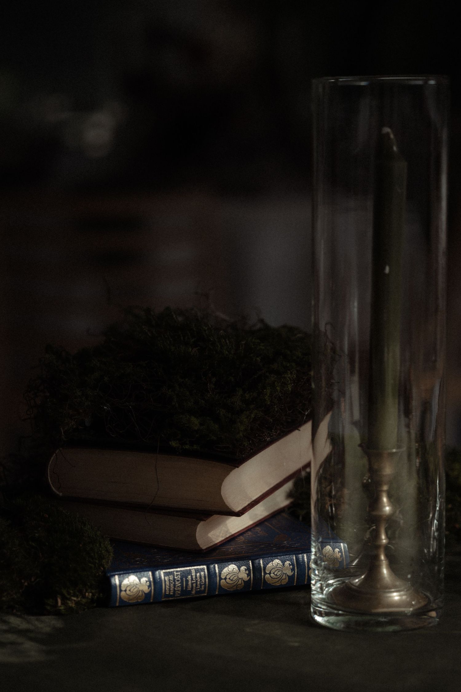 Books cast dramatic shadows against glass containers in a dark moody still life composition.