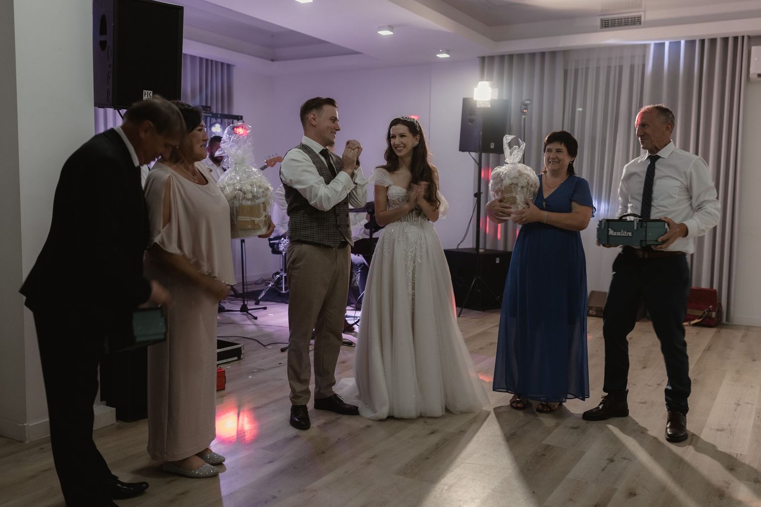 Small group of wedding guests gathered in a dimly lit reception venue while holding drinks and engaged in conversation.
