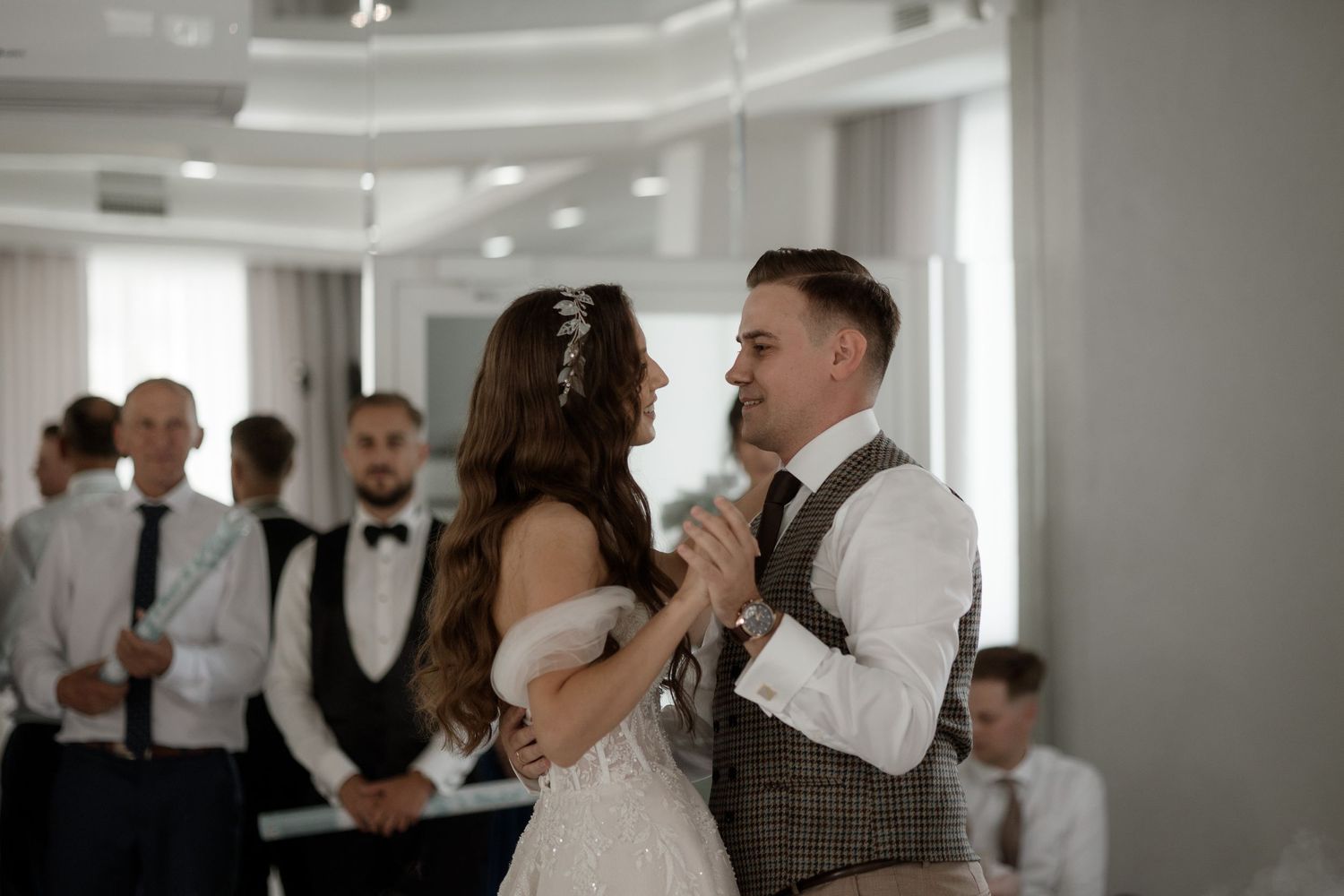 A bride and groom share a romantic moment while dancing at their wedding reception in an elegant white venue.