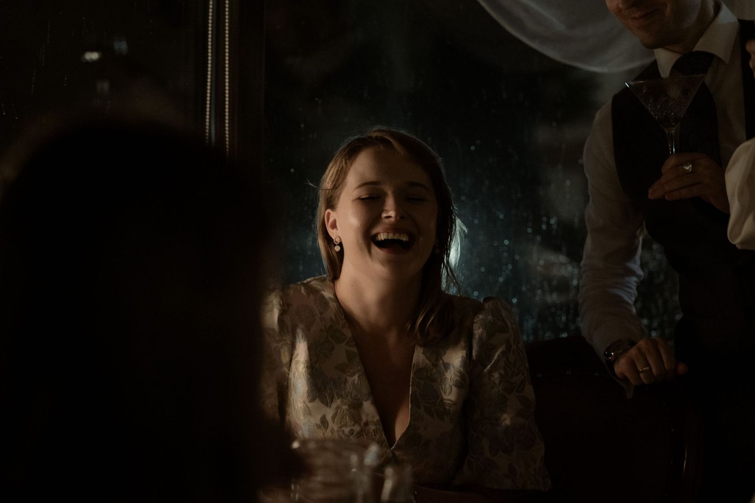 A joyful person laughing while wearing a sparkly gold evening dress in dark atmospheric lighting.