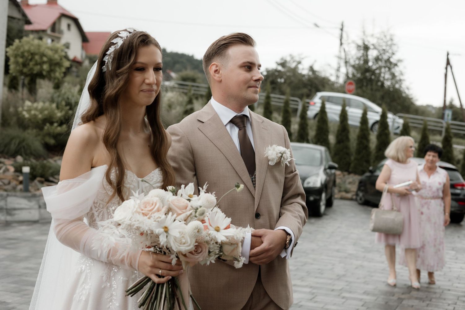 A couple walking together at their outdoor wedding with white floral bouquet.