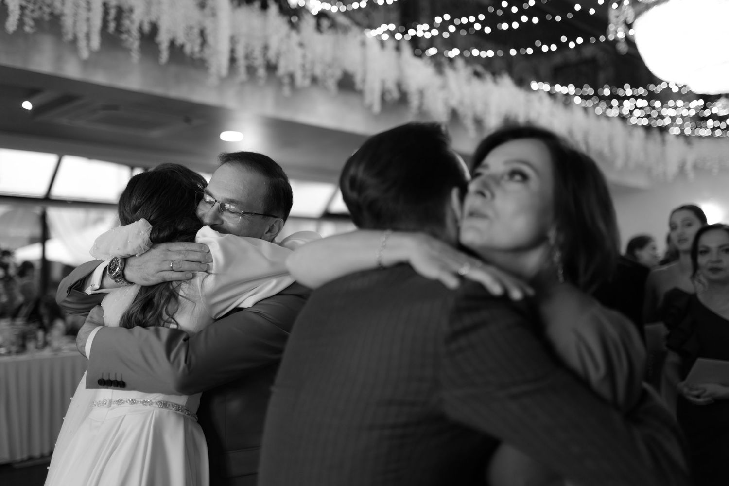 Black and white photo showing couples slow dancing in an intimate reception venue decorated with twinkling lights.