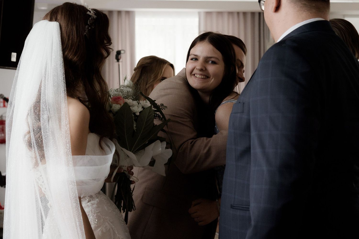 Wedding guests offer warm hugs and congratulations to the bride in her white veil during the reception celebration.