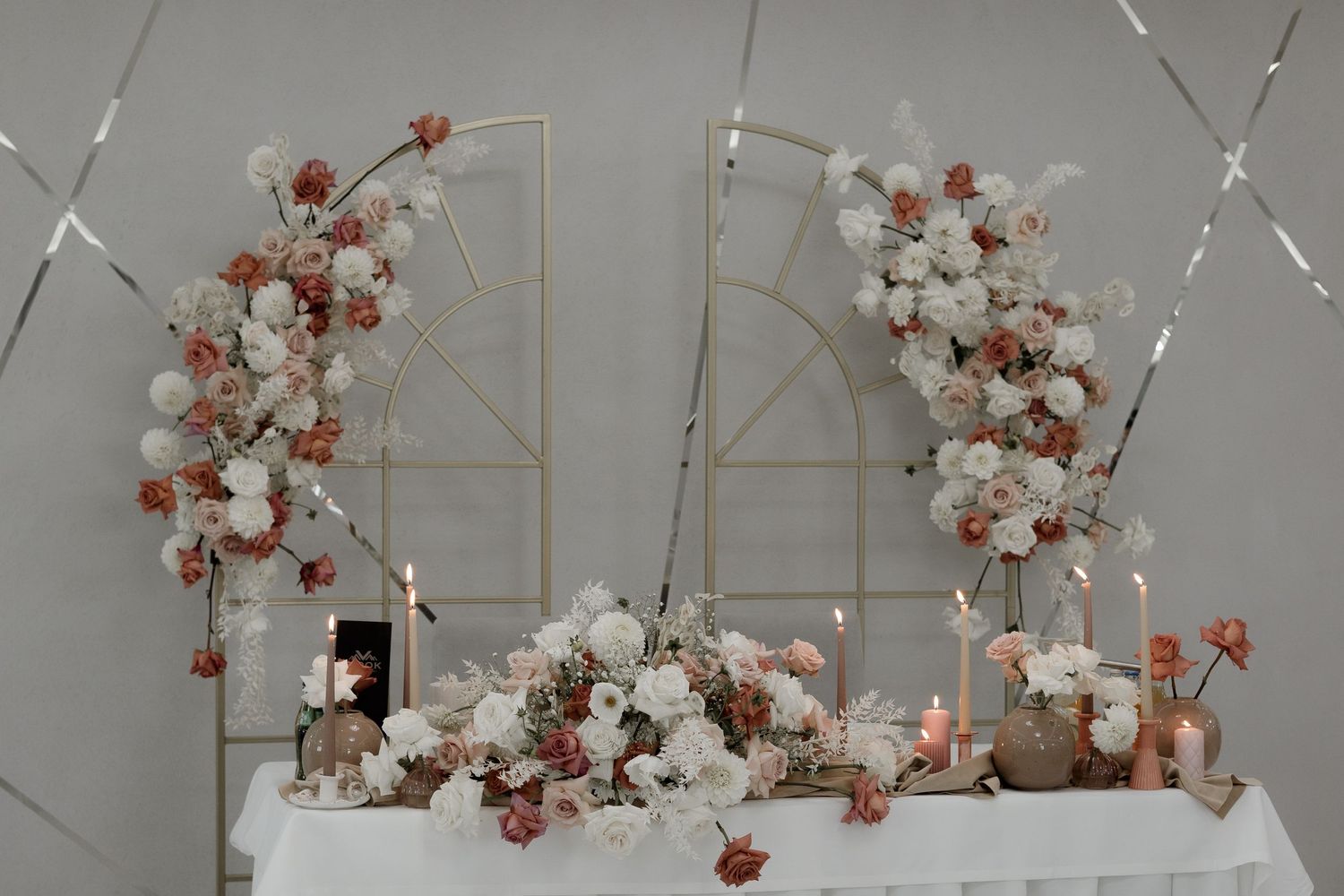 Elegant wedding ceremony setup with white and blush floral arch arrangements and white table decor against mirrored panels.
