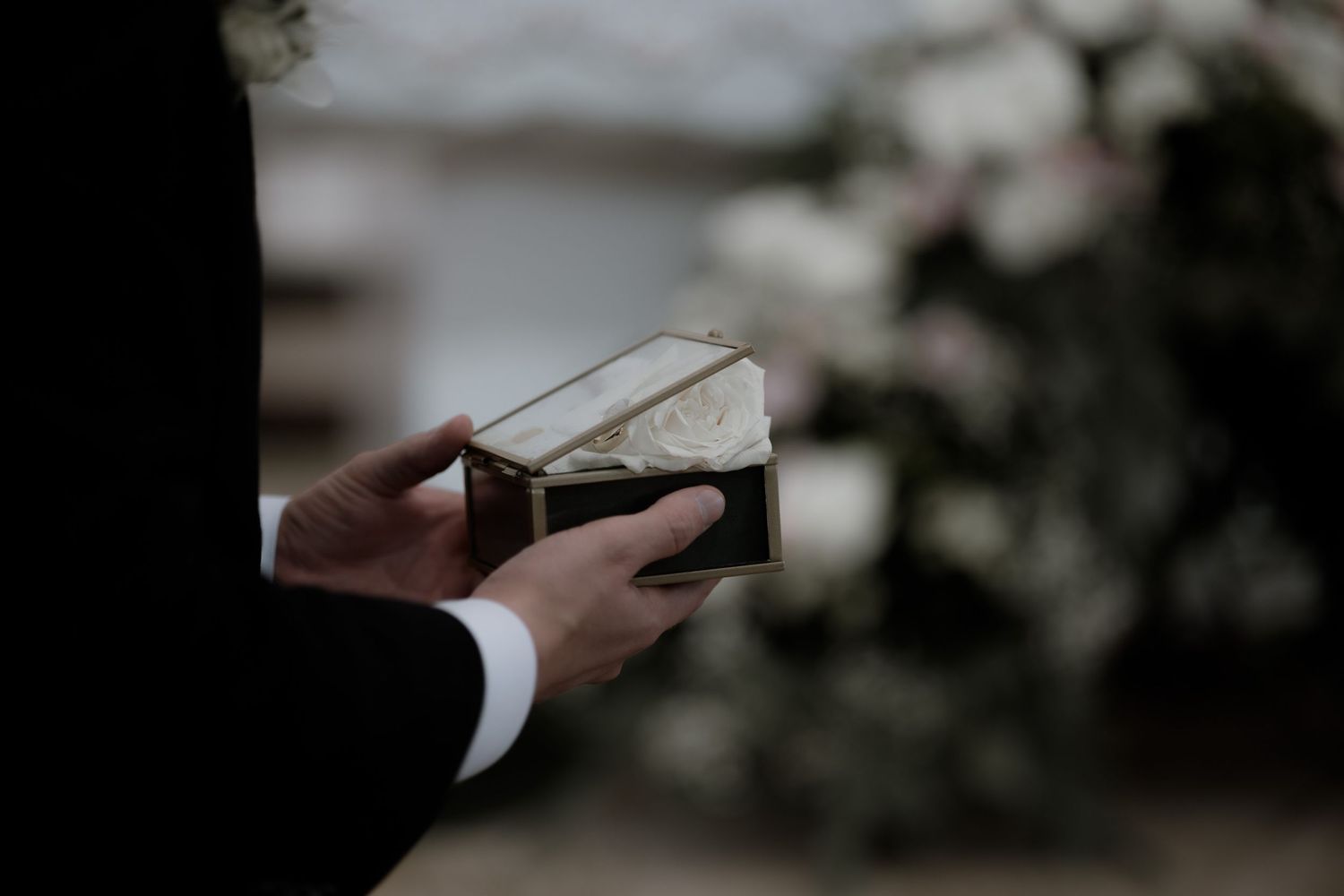 Hands hold an open book during a wedding ceremony with soft blurred floral background.