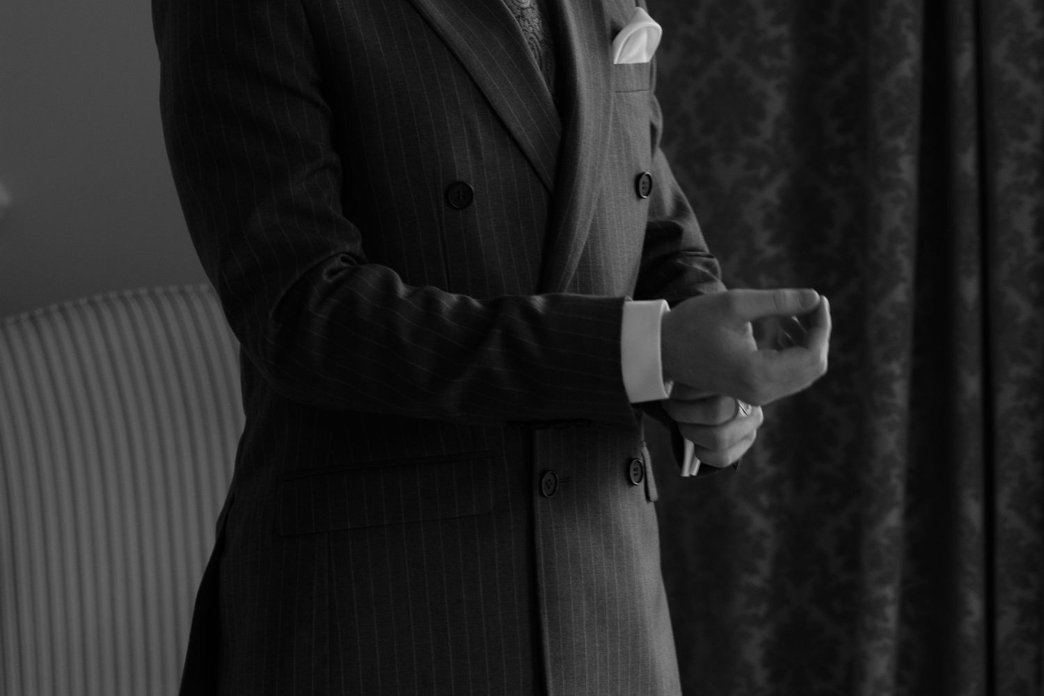 A black and white photograph shows someone wearing a formal suit jacket adjusting their sleeve cuff.
