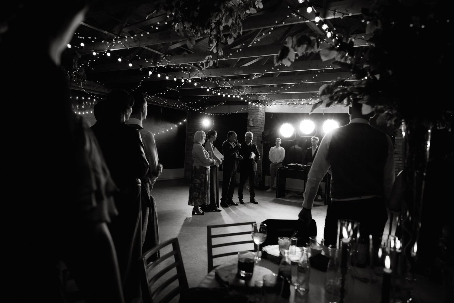 A dimly lit nightclub performance space with stage lights and people silhouetted in the background.