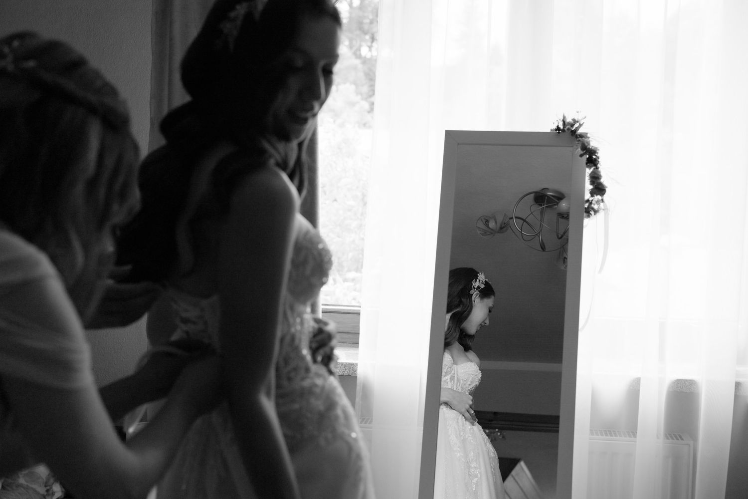 Black and white photo of a bride in a wedding dress looking at her reflection in a mirror before the ceremony.