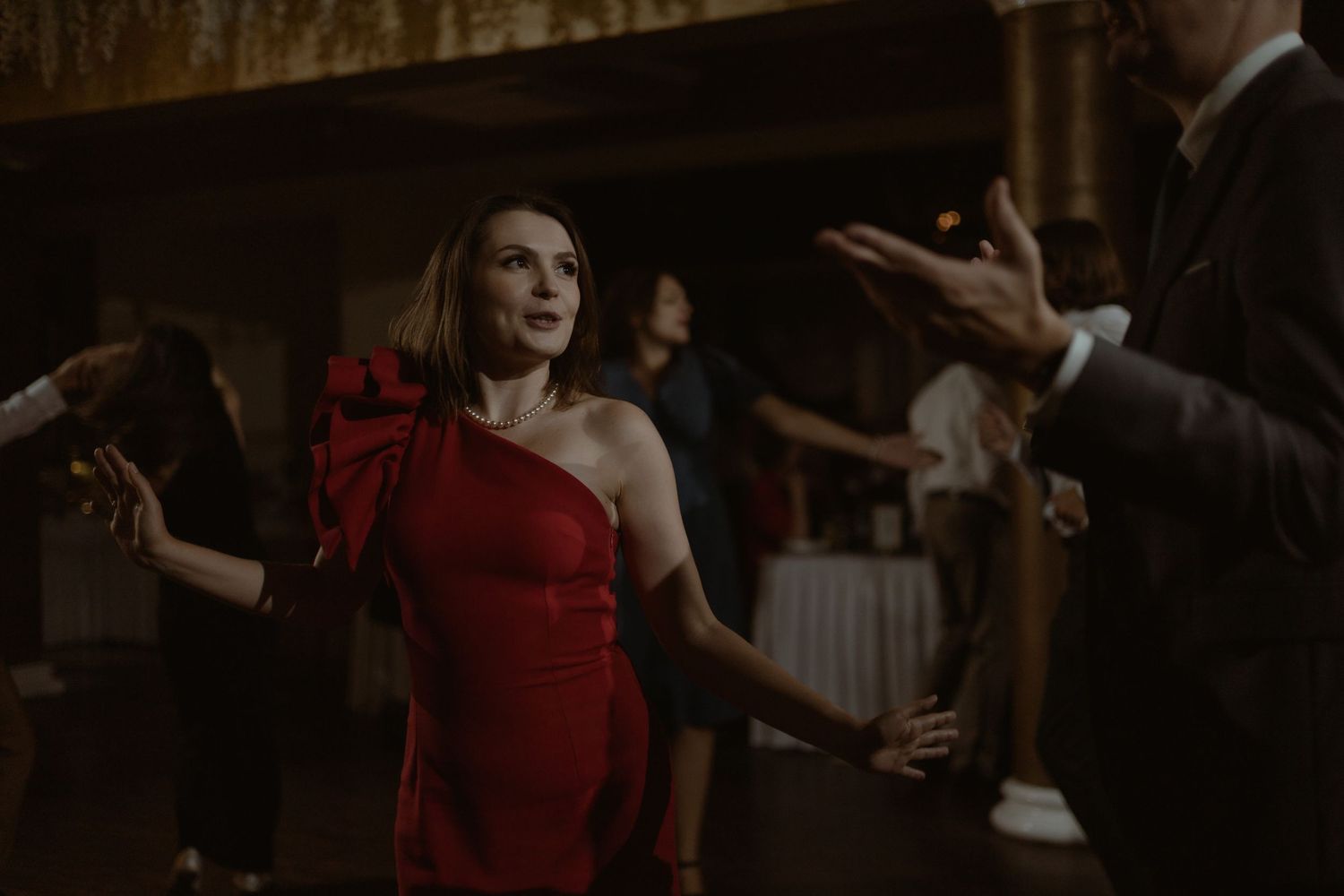 Elegant figure in a red one-shoulder gown dances with dramatic flair in a dimly lit, vintage-style room.